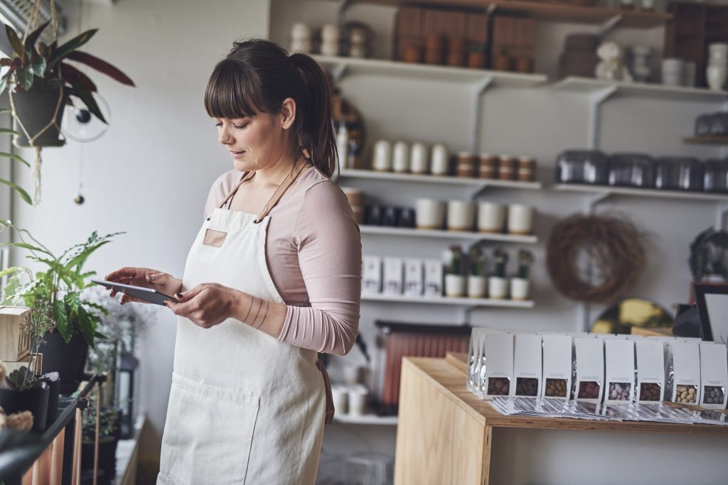 Young female florist checking her online orders with a digital tablet while standing in her flower shop